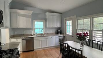 Une cuisine moderne avec des meubles blancs, une table à manger avec des chaises, une cuisinière et une machine à café.