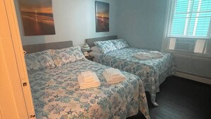 Una camera con due letti, ognuno con biancheria e asciugamani a motivi floreali. Sono presenti due quadri appesi al muro, una lampada a soffitto e una finestra con tende.