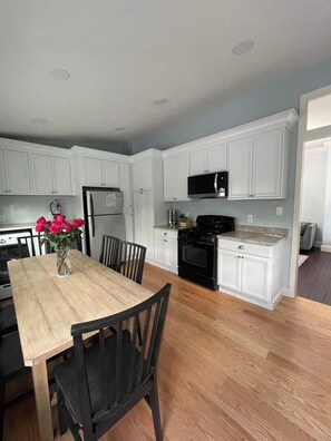 A kitchen with white cabinets, a black stove, and a wooden dining table with chairs. - Newly renovated Kitchen, 1 block from the Beach-1st Floor-Linens&Towels included (Cape May)