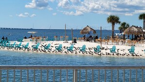 A beach with turquoise chairs, a thatched-roof structure, and palm trees.