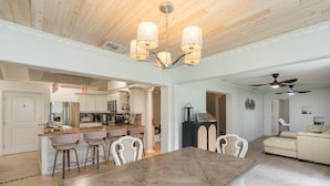 A spacious living area with a wooden dining table, a kitchen with modern appliances, and a ceiling fan.