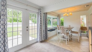 A dining area with a table and chairs, a bench with cushions, and a view of the garden through large windows.