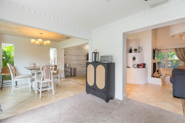 Uma sala ampla com um conjunto de jantar, um armário preto com portas de palha e uma área de estar aconchegante com um sofá e uma TV.
