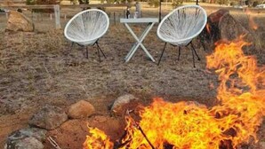 A campfire with rocks around it, two white chairs, and a table in an outdoor setting. - Saje Farm by Your Innkeeper Mudgee (Cooks Gap)