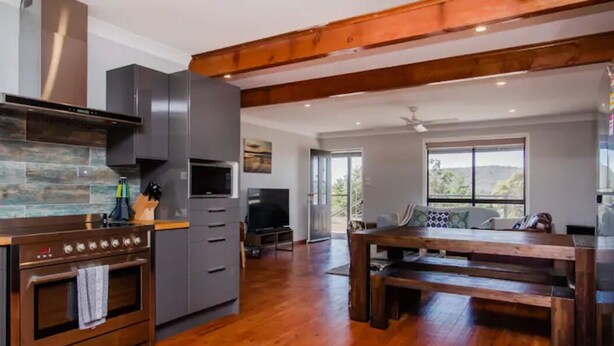 A modern kitchen with a built-in oven, grey cabinets, and a wooden dining table. - Saje Farm by Your Innkeeper Mudgee (Cooks Gap)