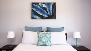 A neatly made bed with a striped bedspread, two pillows, and a decorative pillow. There are two bedside tables with lamps on either side of the bed. - Saje Farm by Your Innkeeper Mudgee (Cooks Gap)