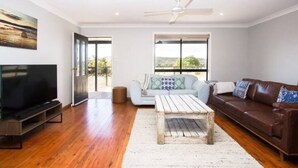 A spacious living room with a flat-screen TV, a ceiling fan, a light-colored sofa, a brown leather couch, and a rustic coffee table. - Saje Farm by Your Innkeeper Mudgee (Cooks Gap)