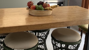 A kitchen with a wooden countertop, a fruit bowl, wicker chairs, and pendant lights.