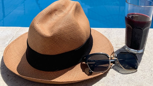 A poolside setting with a hat, sunglasses, and a drink on a table.