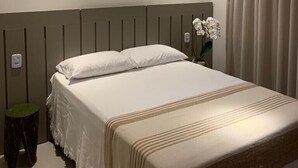 A modern hotel room with a large bed, a small stool, and a potted orchid.