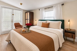 Ein Hotelzimmer mit einem Bett, einem Sessel, einem Nachttisch, einer Lampe und einem Fenster mit Vorhängen.