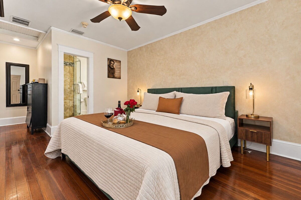 Una habitación de hotel con una cama grande, un ventilador de techo, una mesita de noche con lámpara y un aparador de madera.