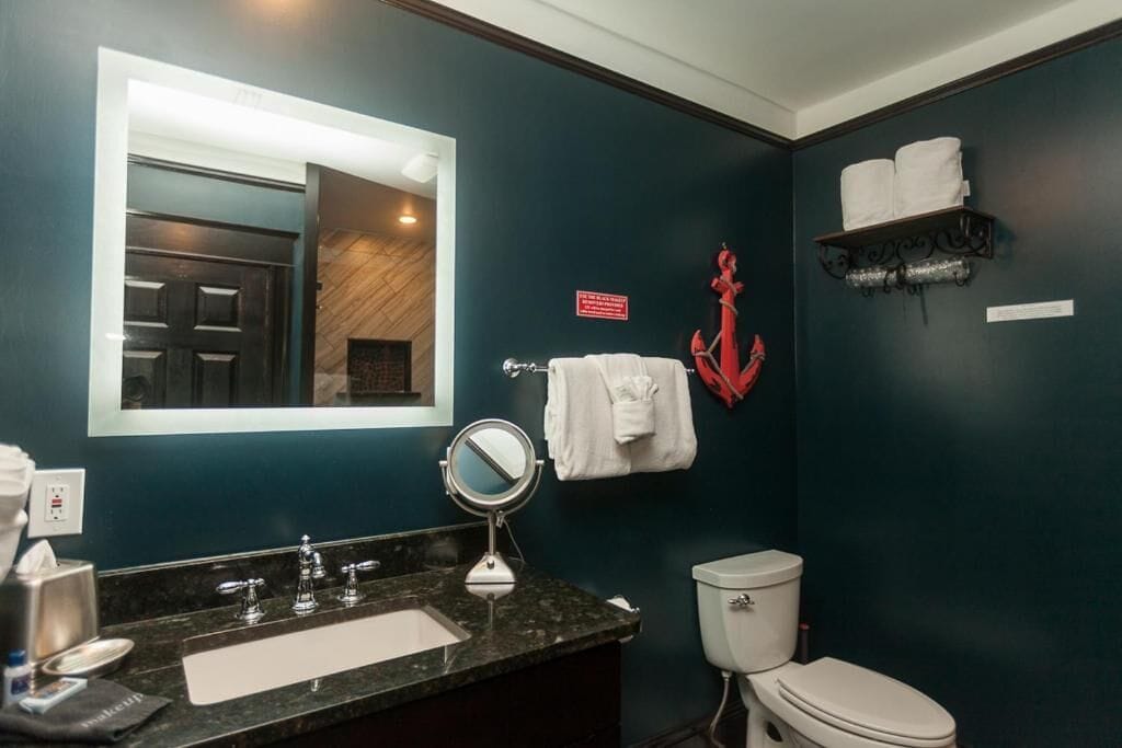 Une salle de bain avec un mur bleu foncé, un lavabo blanc avec un miroir, des toilettes et un porte-serviettes avec des serviettes.