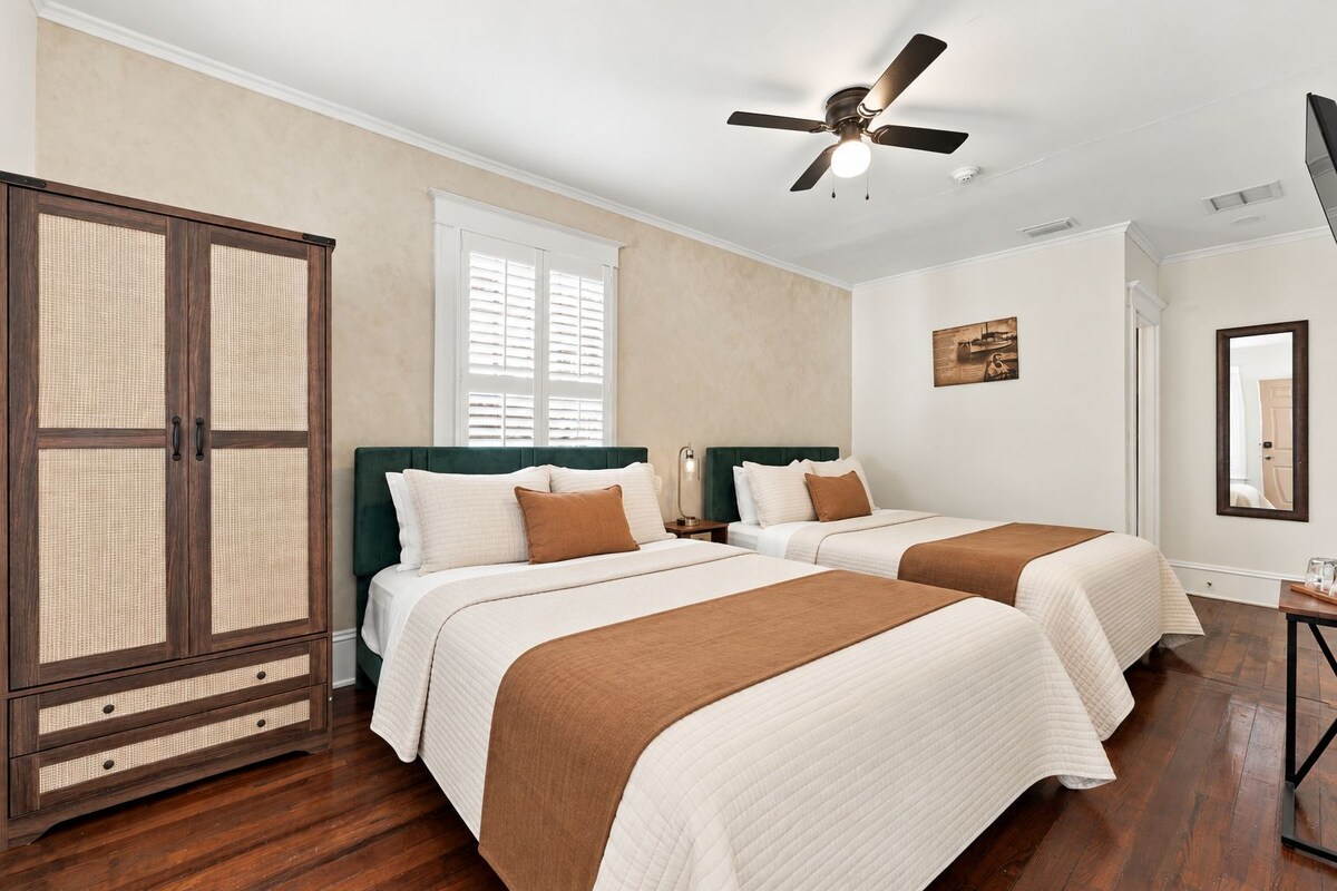 A hotel room with two beds, a large wardrobe, a ceiling fan, and a window with blinds.