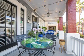 A covered outdoor patio with a round glass table, chairs, and a wicker basket. - Hemingway House Boutique Hotel (St. Augustine)