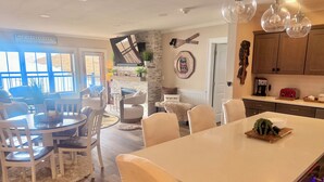 A modern kitchen with a large island, wooden cabinets, and a dining area with white chairs.