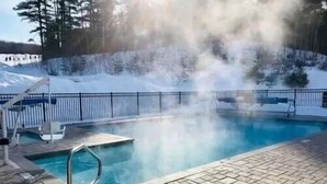 A swimming pool with a hot spring feature, surrounded by a snow-covered landscape and a metal fence.