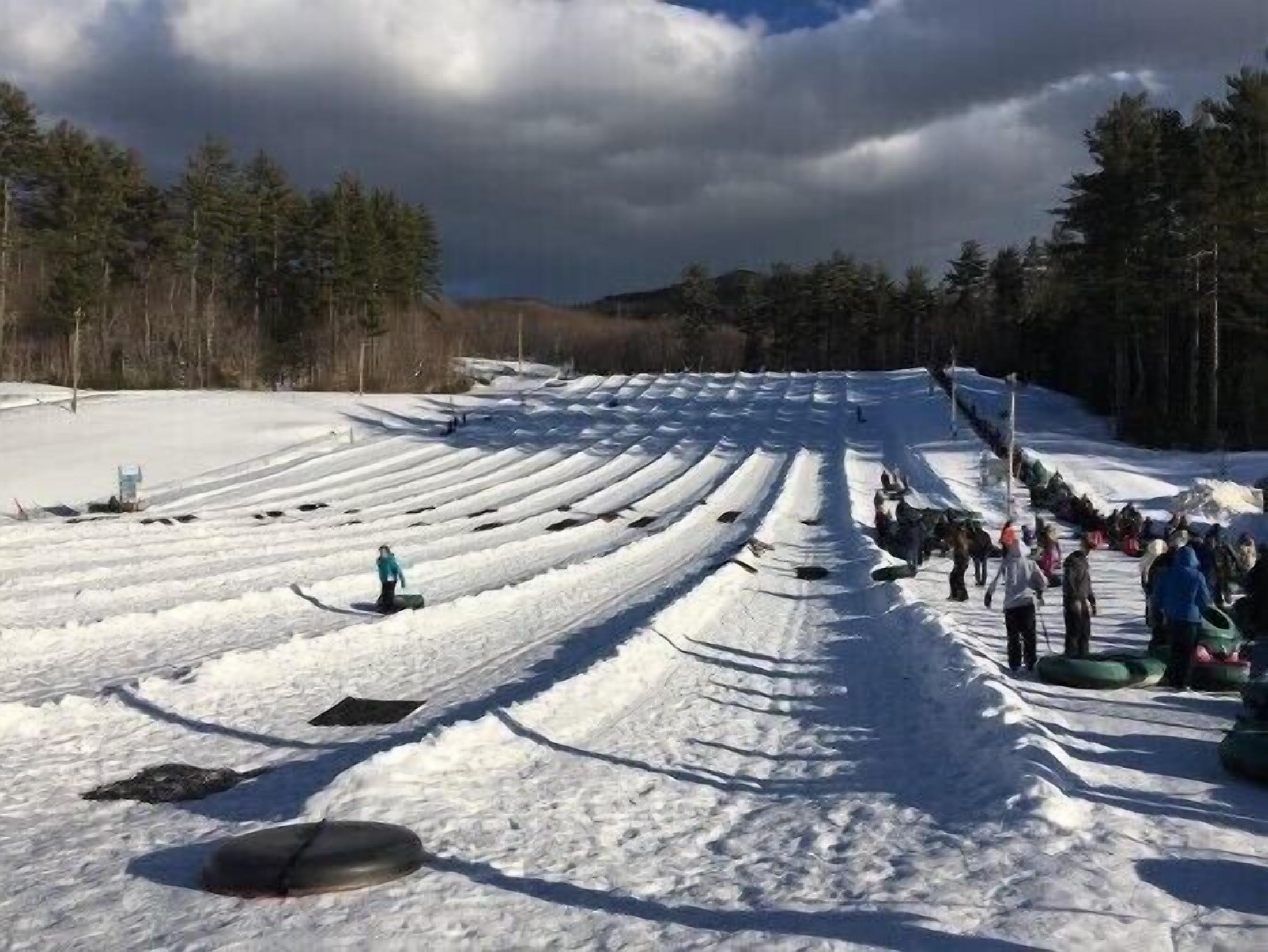 A snowy ski slope with marked lanes and a group of people gathered at the bottom.
