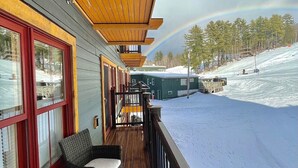 A wooden deck with wicker furniture, overlooking a snowy landscape and a ski lift.