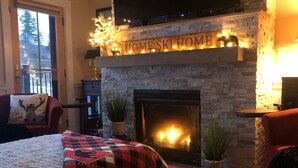 A cozy room with a fireplace, a bed with a plaid blanket, and a sign above the fireplace that reads "HOME SKI HOME".