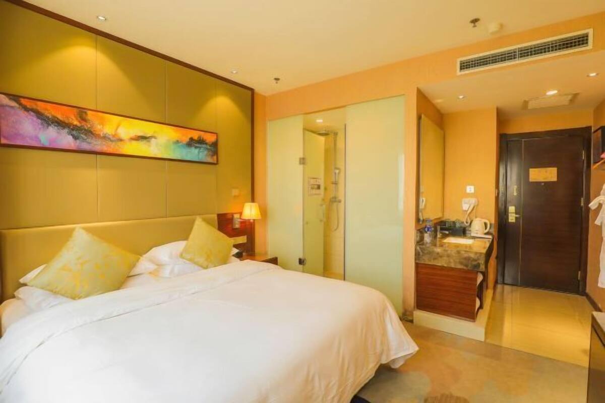 Une chambre d’hôtel comprenant un lit, une table de chevet, un tableau, une salle de bain et une kitchenette.