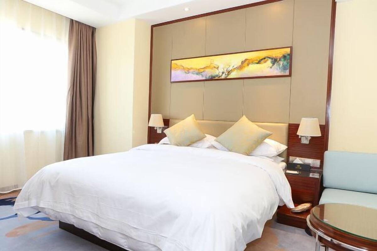 Une chambre d’hôtel avec un grand lit, un tableau au mur et un coin salon avec une table.