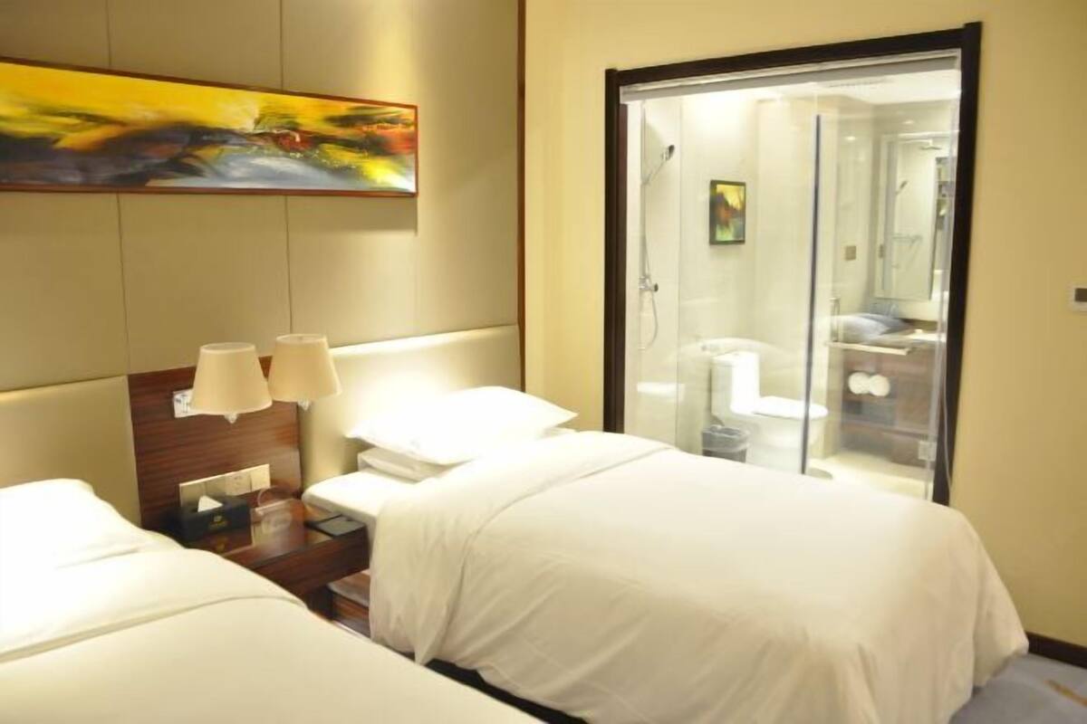Une chambre d’hôtel avec deux lits, une douche en verre, un tableau au mur et une table de chevet avec des lampes.