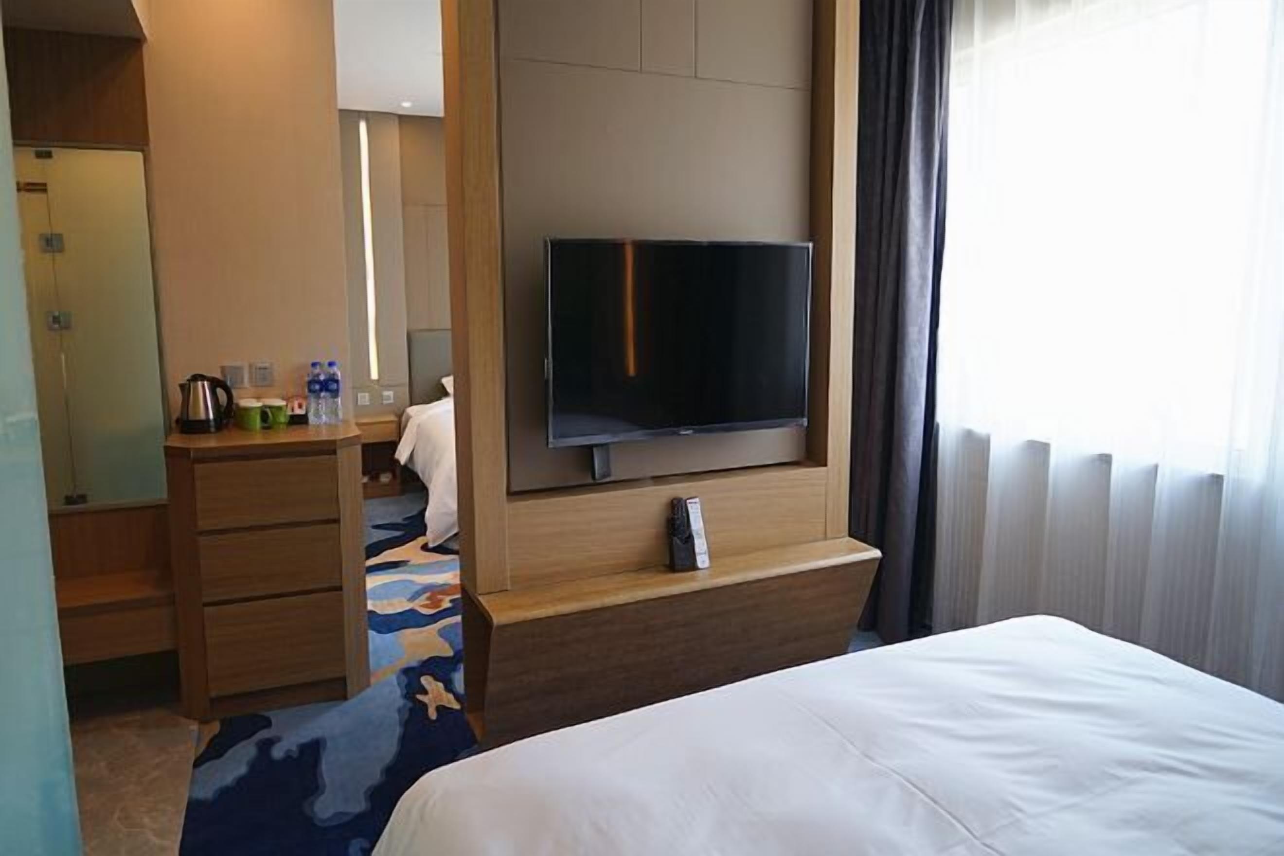 A hotel room with a bed, a TV mounted on the wall, a desk with a chair, and a bathroom with a mirror and towel rack.