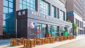 A building with a sign that reads "阿里巴巴大街" and "东风大街". There are outdoor tables and chairs in front of the building. - Zhongji Garland Hotel (Tianjin)
