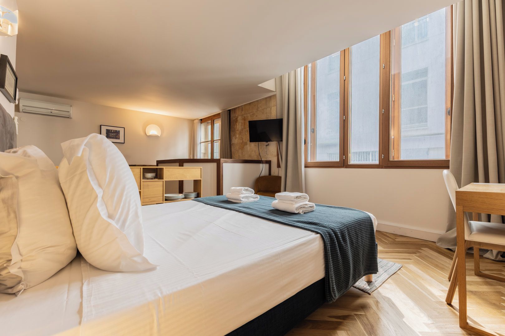 A hotel room with a bed, a desk, a chair, a TV, and a window with curtains.