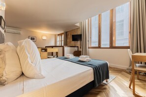 A hotel room with a bed, a desk, a chair, a TV, and a window with curtains.
