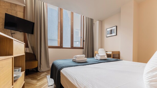 A hotel room with a bed, a TV, a desk, a chair, and a window with curtains. - Magnificent Bordeaux studio in beautiful stone in the heart of the city (Bordeaux)