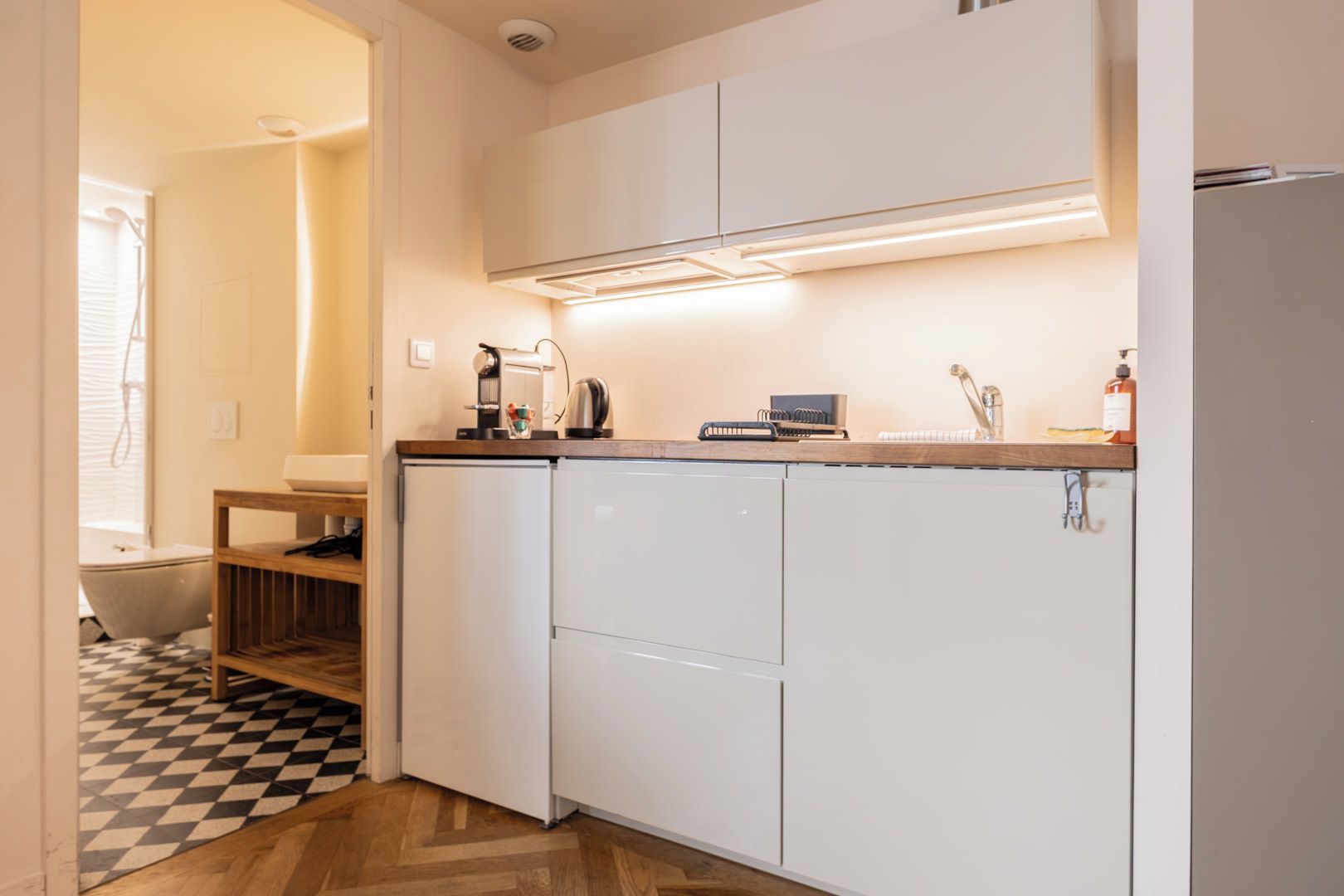 A compact kitchen with white cabinets, a built-in oven, a coffee maker, and a kettle on the countertop.