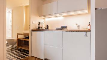 A compact kitchen with white cabinets, a built-in oven, a coffee maker, and a kettle on the countertop.