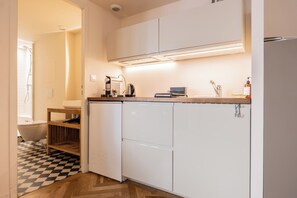 Cocina compacta con armarios blancos, horno integrado, cafetera y hervidor sobre la encimera.