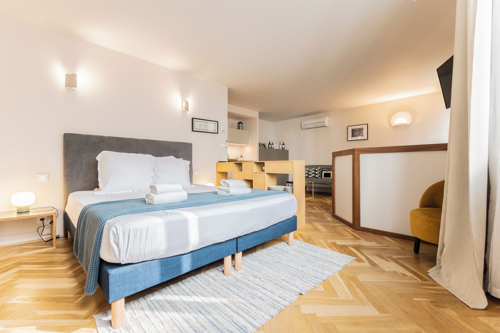 Quarto de hotel moderno com cama, mesa de cabeceira e pequena escrivaninha.