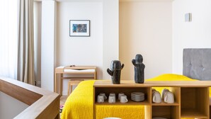 A hotel room with a bed, a desk, a chair, a picture on the wall, and a shelf with mugs and plates. - Magnificent Bordeaux studio in beautiful stone in the heart of the city (Bordeaux)