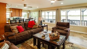 A spacious living room with a brown leather sofa, a coffee table, and a view of a lake through large windows. - Lake Granbury Fishing Escape w/ Dock & Kayaks! (Granbury)