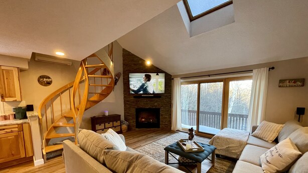 A cozy living room with a wooden spiral staircase, a fireplace, and a large TV. - An Amazing Mountain Getaway! (Bartlett)