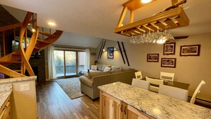 A modern kitchen with wooden cabinets and a marble countertop, a dining area with white chairs, and a cozy living room with a sofa and a fireplace. - An Amazing Mountain Getaway! (Bartlett)