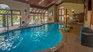 An indoor swimming pool with a stone wall, wooden ceiling beams, and a view of the outdoors. - An Amazing Mountain Getaway! (Bartlett)