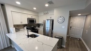 A modern kitchen with white cabinetry, stainless steel appliances, a marble countertop, and a clock on the wall. - OCEANFRONT 2 BD, 2.5 BTH in SURFSIDE! (Surfside Beach)