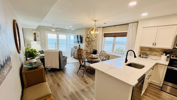 A modern kitchen with a central island, wooden flooring, and a view of the ocean through large windows. - OCEANFRONT 2 BD, 2.5 BTH in SURFSIDE! (Surfside Beach)