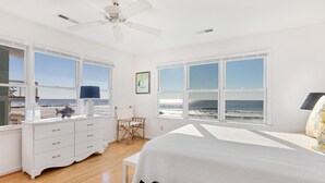 Une chambre avec un grand lit, une commode blanche, une chaise et une vue sur l’océan.