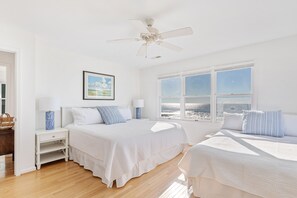 A bedroom with two beds, a ceiling fan, a window with a view, and a nightstand with a lamp.