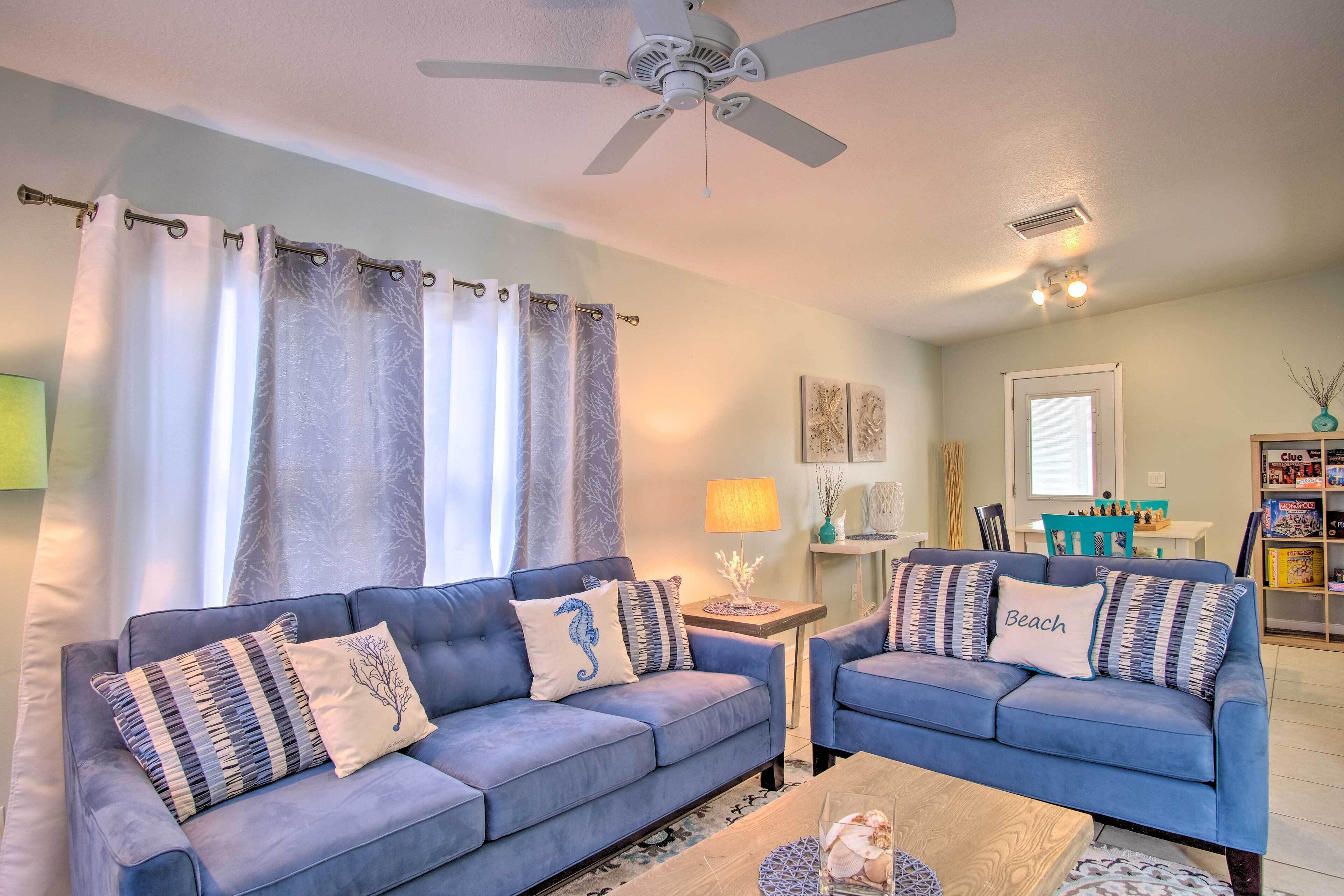 A living room with two blue sofas, a ceiling fan, a coffee table, and a lamp.