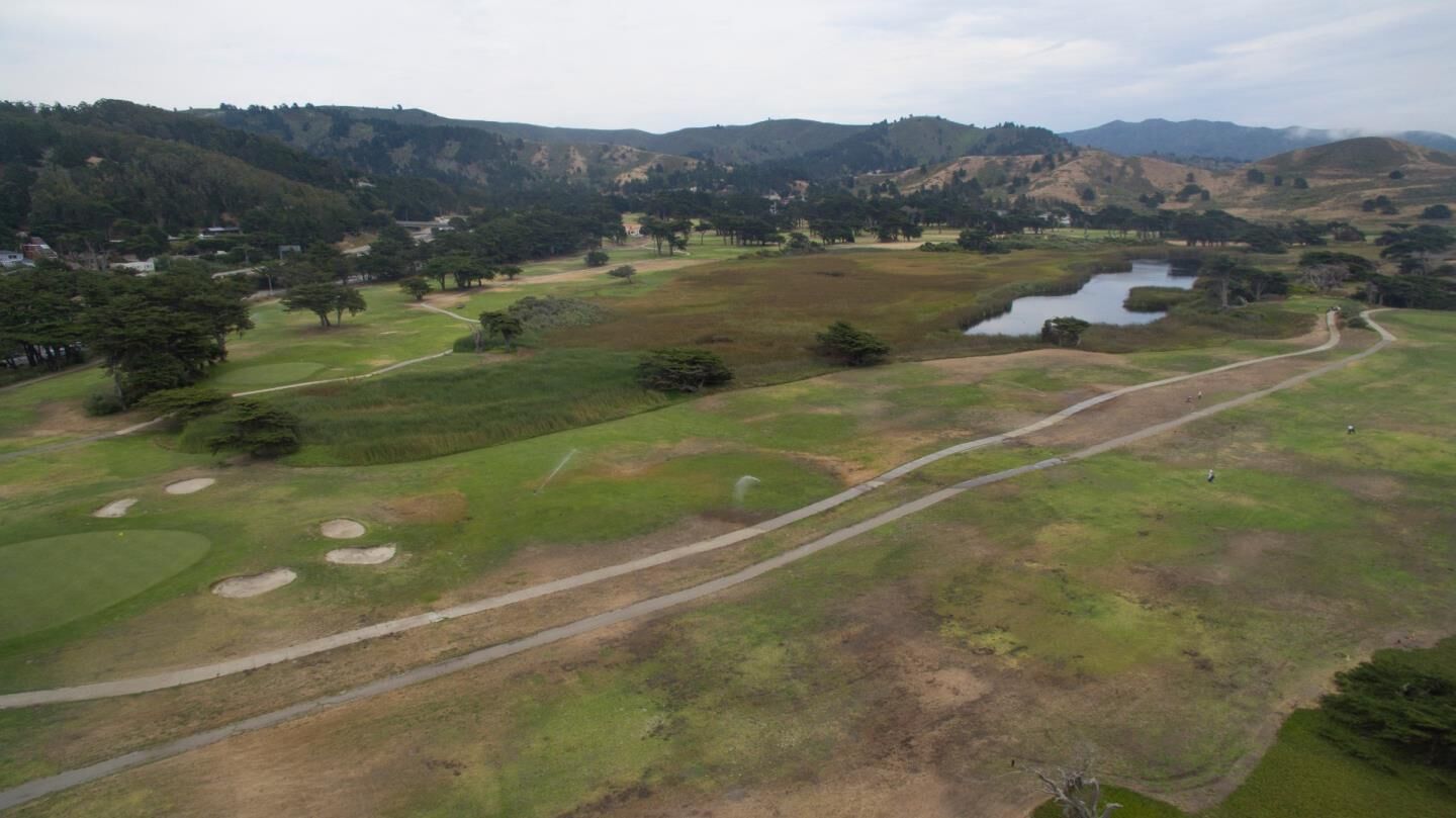 An aerial view of a golf course with multiple fairways, sand traps, and a pond.