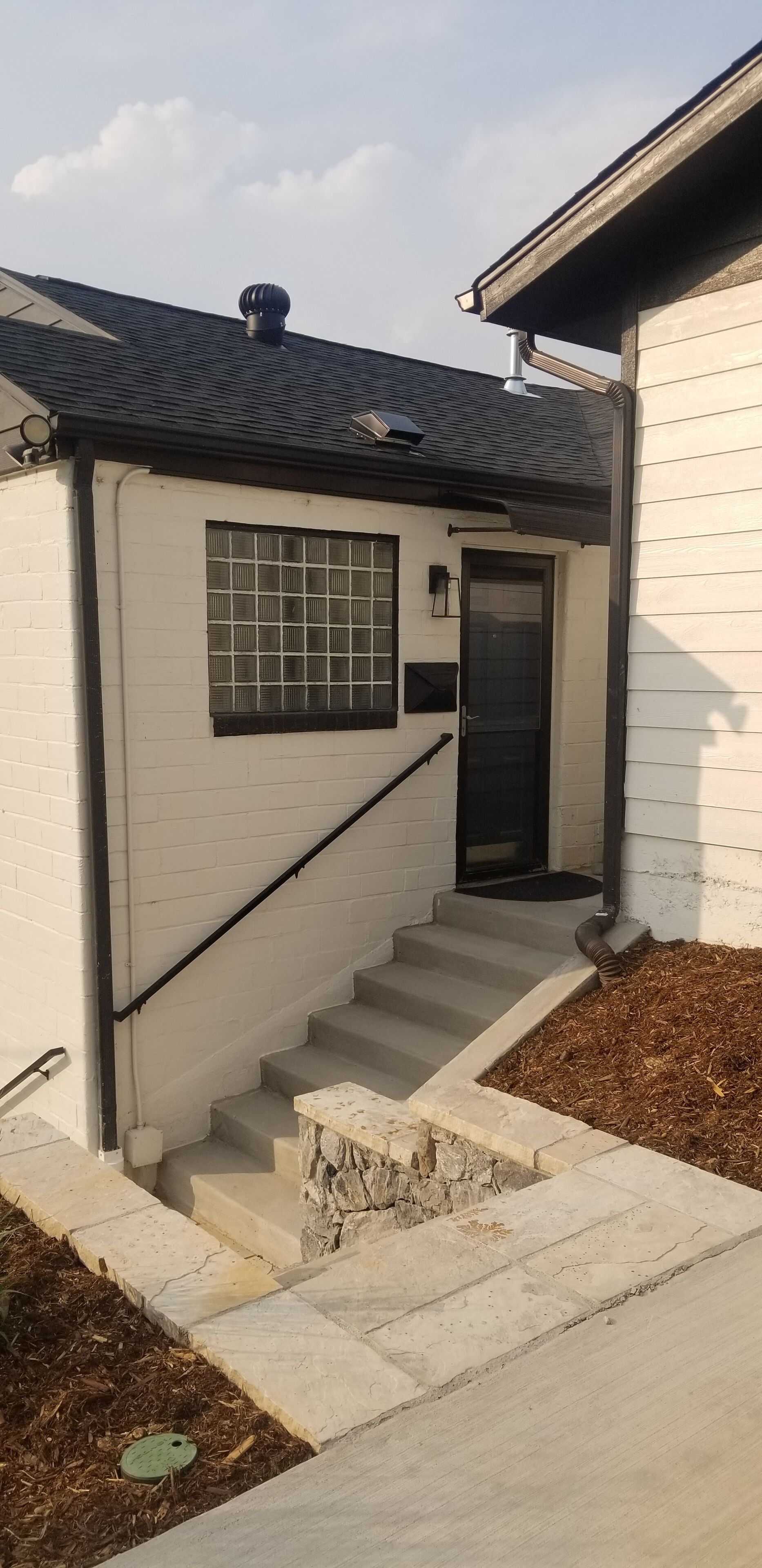 A house with a white exterior, a black door, and a small window. There is a set of concrete steps leading to the door.