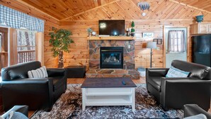 A cozy cabin interior with a stone fireplace, two leather sofas, a coffee table, and a ceiling fan. - Close ‘n Secluded❤️Mountain Views*PRIVATE RESORT*Hot Tub*Cabin😊A+++ (Sevierville)