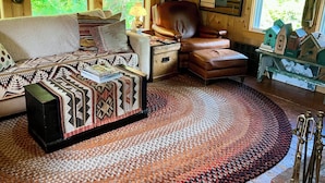 Ein gemütlicher Raum mit einer Couch, einem Ledersessel, einem gemusterten Teppich und einem Holztisch mit Dekoration.